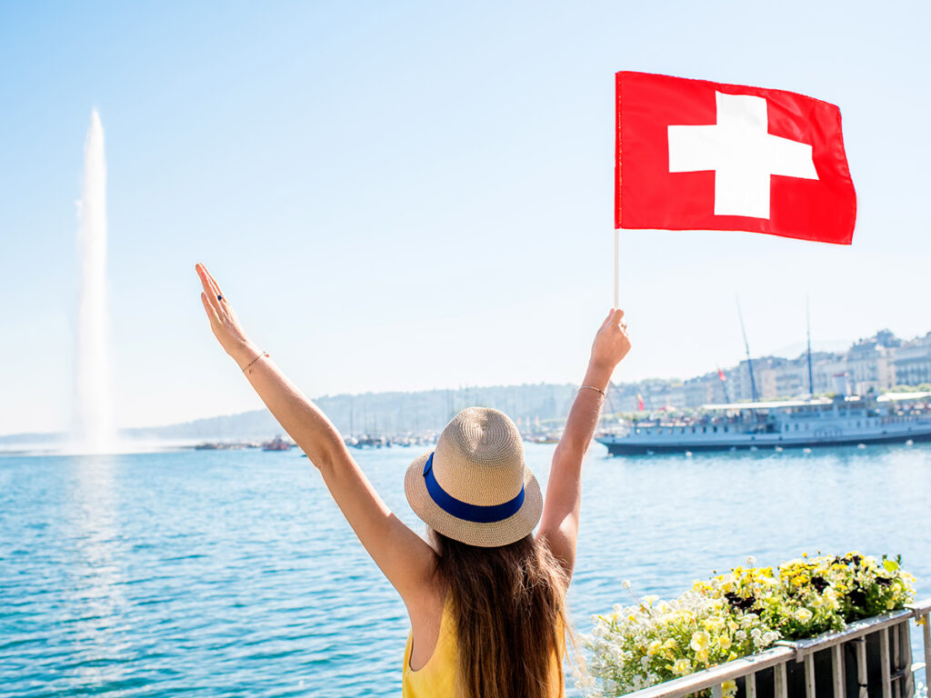 Jeune fille de dos devant le lac de Genève portant un drapeau suisse