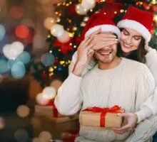 Jeune femme offrant un cadeau surprise à son mari, qui ferme les yeux, célébrant Noël à la maison.