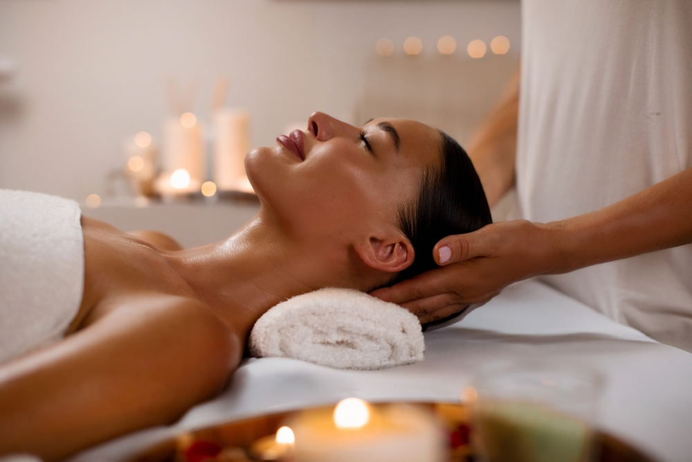 Femme détendue recevant un massage de la tête pour la fête des mères par un masseur professionnel, se reposant dans un spa moderne de luxe dans une atmosphère calme et sereine, vue de côté.