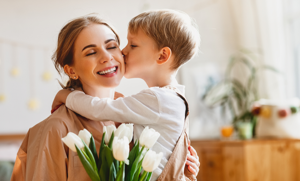 Un fils embrasse sa mère heureuse et lui donne un bouquet de tulipes à l'occasion de la fête des mères lors d'une célébration à la maison.