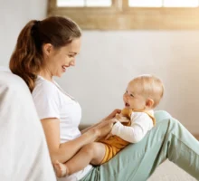 Jeune maman caucasienne tenant son bébé dans les bras et qui embrasse son adorable petit garçon, posant ensemble à la maison.