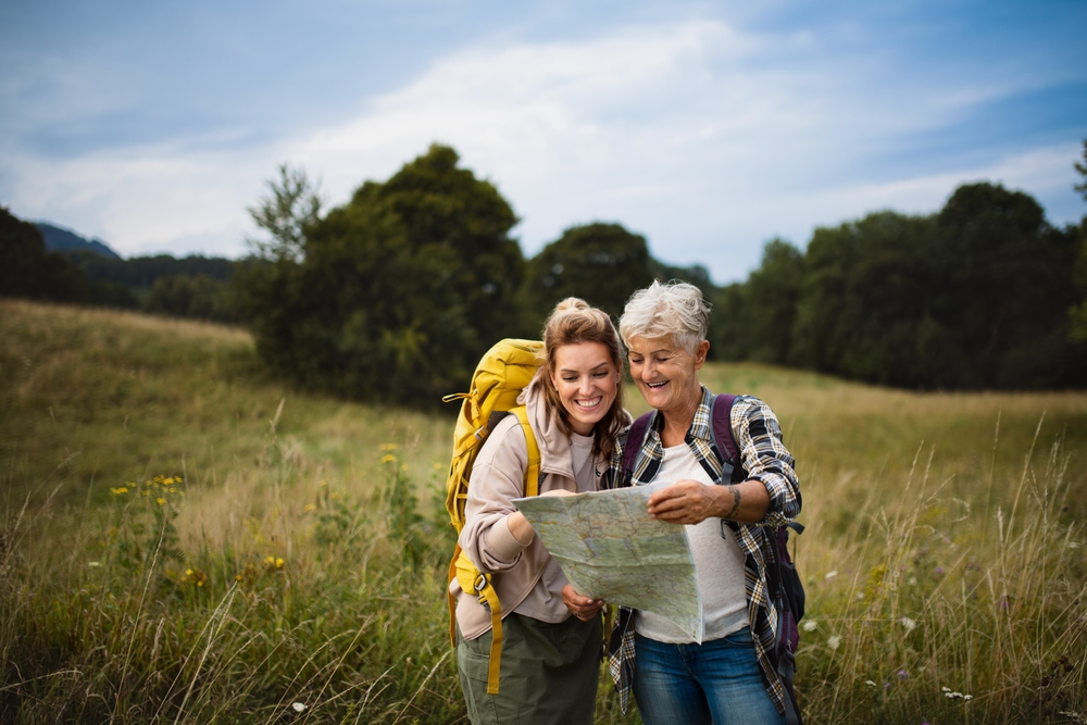 Une femme heureuse et une mère active et âgée font de la randonnée et regardent la carte en plein air, dans la nature.