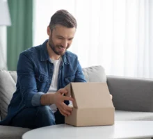 Un jeune papa heureux assis sur son canapé qui ouvre son cadeau à l'occasion de la fête des pères.