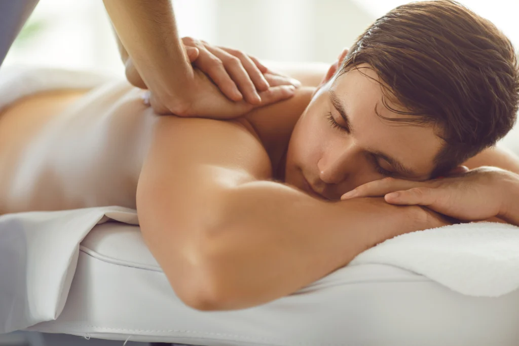 Gros plan d'un homme se faisant masser par un professionnel dans un salon de spa ou un centre de bien-être. Jeune homme allongé sur un lit, les yeux fermés, profitant d'un massage du dos effectué par un masseur qualifié à l'occasion de la fête des pères.