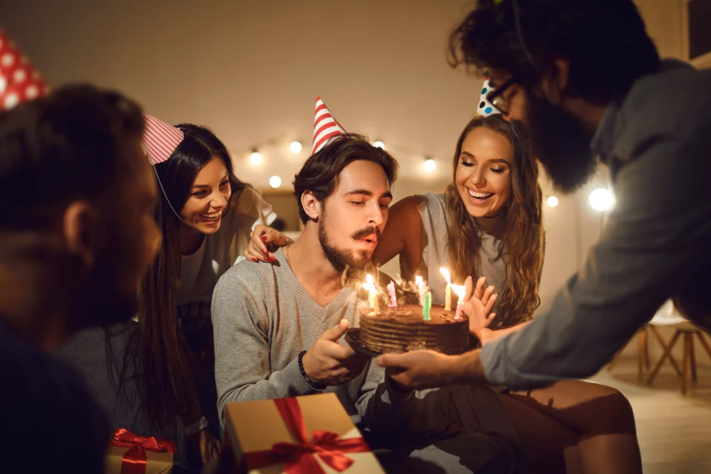 Jeune homme souriant les yeux fermés, faisant un vœu devant un gâteau d'anniversaire avec des bougies allumées.