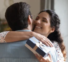 Une jeune femme tenant un coffret cadeau avec un nœud ravie embrassant son mari, le remerciant pour son cadeau d'anniversaire.