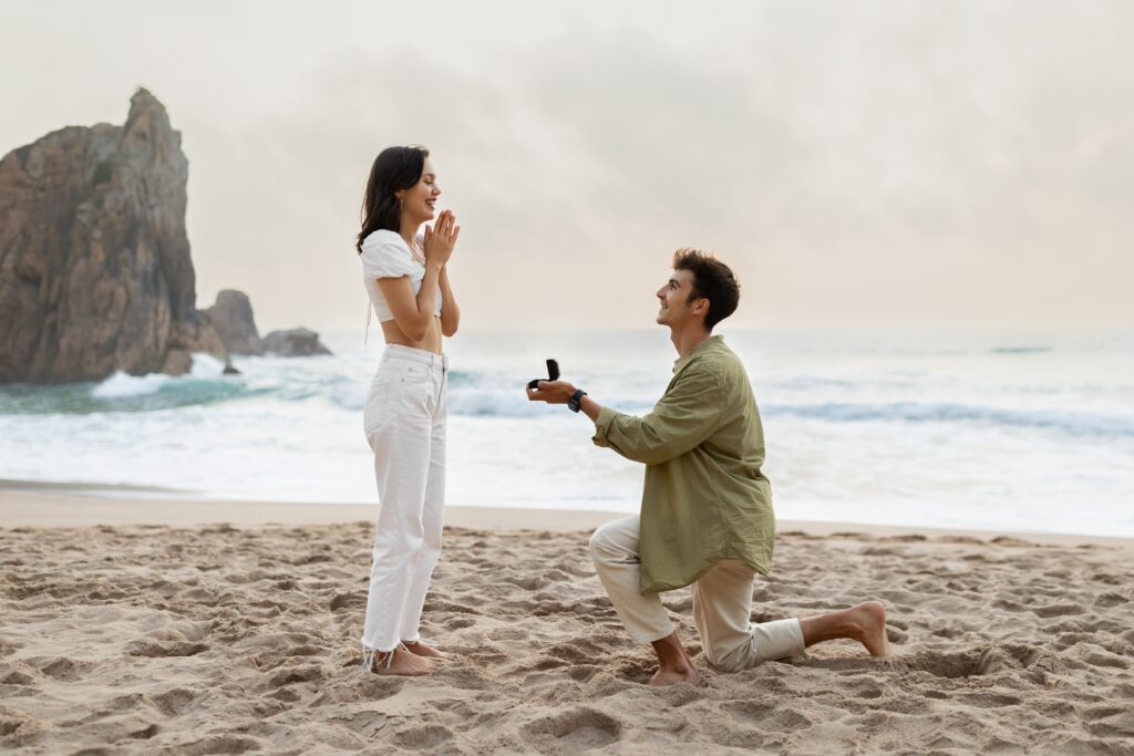 Demande en mariage romantique au bord de la mer. Jeune homme amoureux avec une bague de fiançailles faisant sa demande à une femme heureuse sur une plage au bord de la mer, vue de côté.