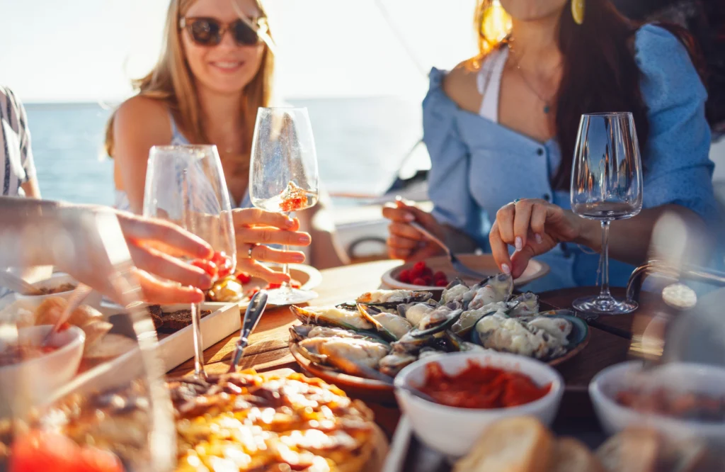 Banquet festif à bord du navire. Gros plan sur une table garnie de mets délicieux. De jeunes femmes souriantes lèvent leur verre de vin ou de cocktail. Enterrement de vie de jeune fille amusant sur un bateau. Déjeuner pendant une croisière en mer.