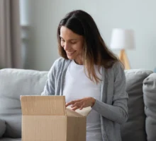Souriante jeune femme déballe une boîte en carton, regarder à l'intérieur, heureux obtenir un cadeau à l'occasion du black friday.