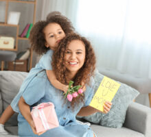 Hija abrazada y dándole regalos a su madre en un sofá