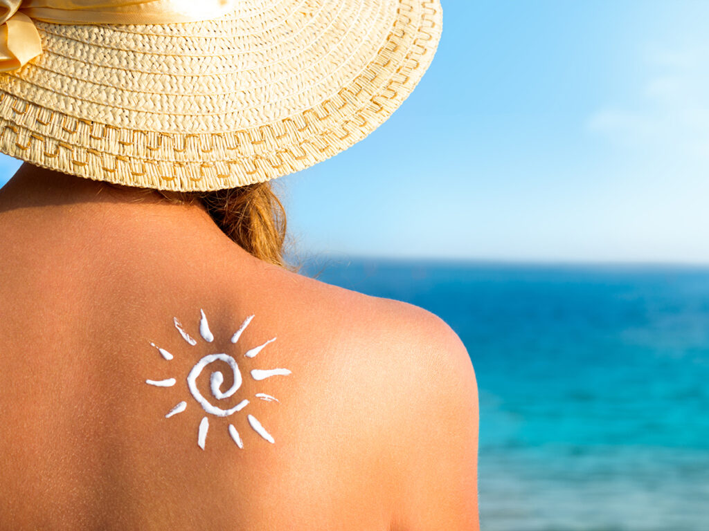 Mujer en la playa de espaldas con un sol dibujado con la crema solar