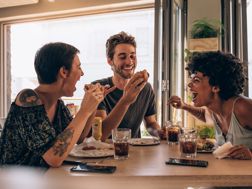 Tres amigos riendo comiendo en un restaurante