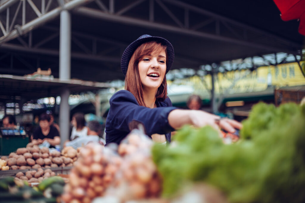 Femme au marché devant les fruits et légumes